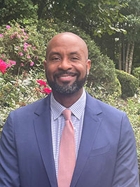 Mason associate professor Drew Richardson is a black man wearing a blue suit, pink tie in front of a natural background