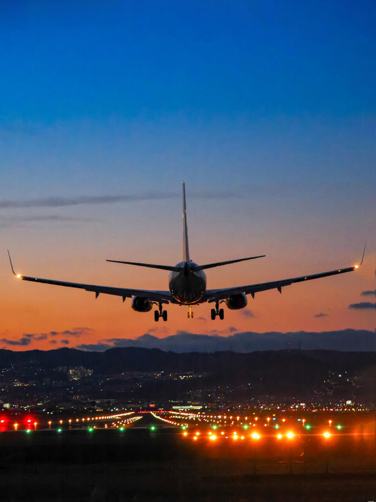 An airplanes wheels goes down to the tarmac of an airport while the sun sets in the background